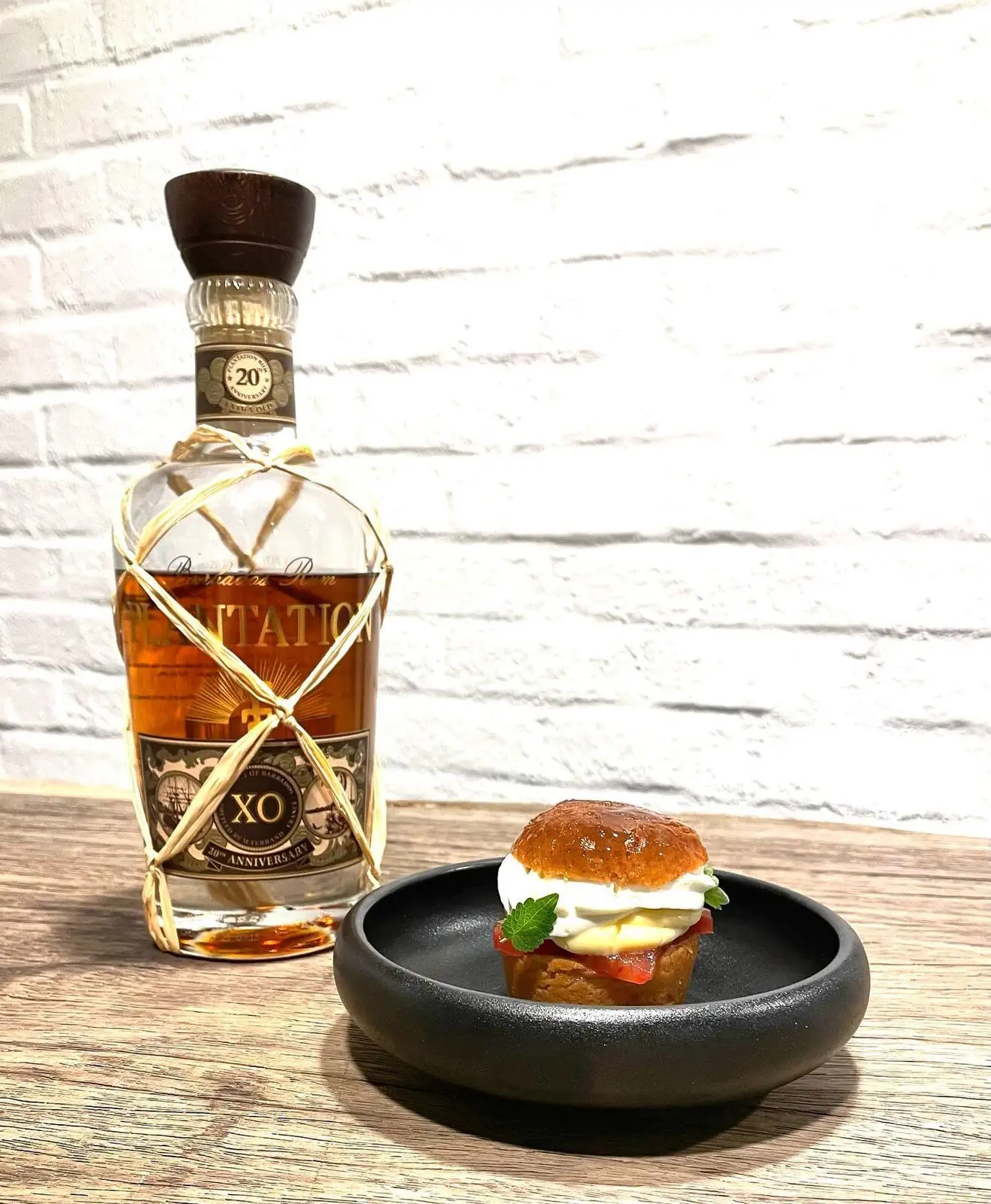 Baba au rhum dressé dans une assiette creuse foncée.
