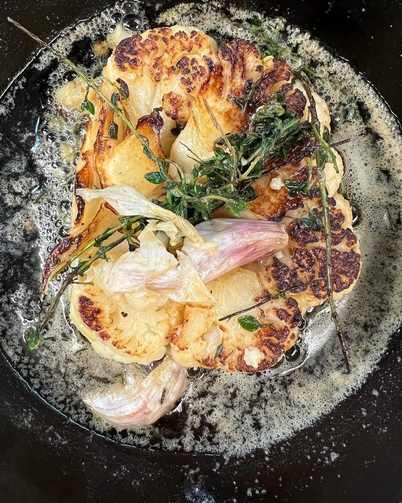 Tranche de chou-fleur rôtie dans un plat noir, herbes et oignons.
