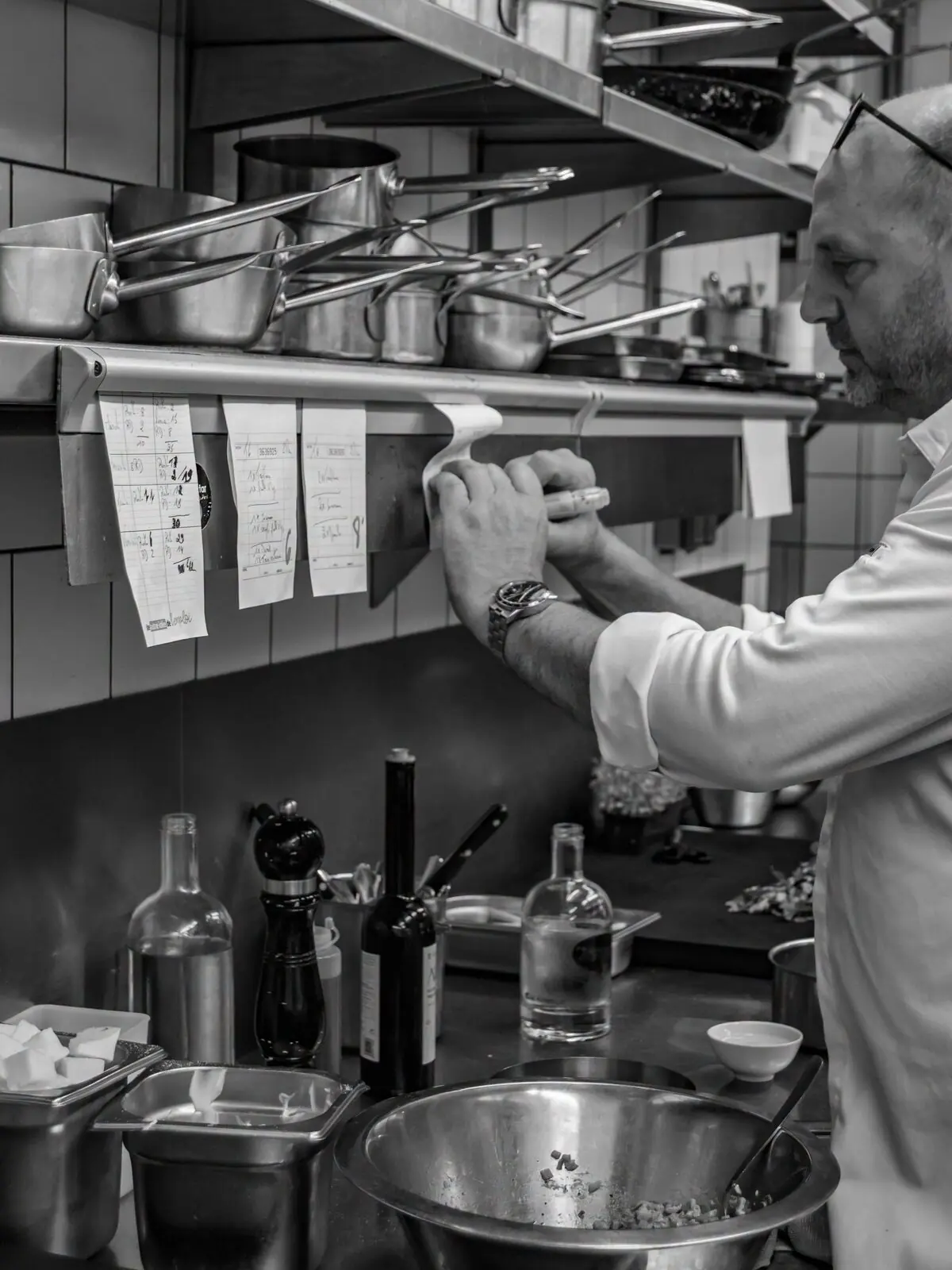 Un cuisinier au passe, en cuisine, photographié en noir et blanc.