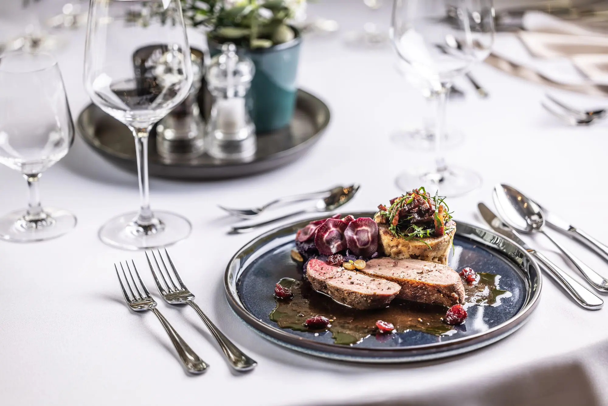 Table dressée en salle : verres, argenterie et une assiette de gibier.